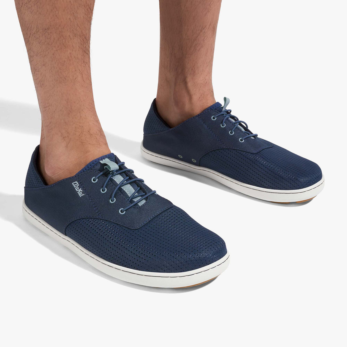 Navy blue lace-up shoes with white soles and textured fabric upper, worn on male feet.