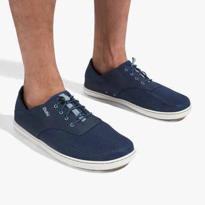 Navy blue lace-up shoes with white soles and textured fabric upper, worn on male feet.