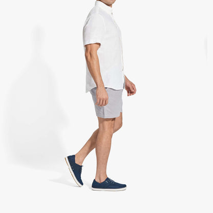 Man wearing white short-sleeve button-up shirt, light blue shorts, and dark blue canvas sneakers.