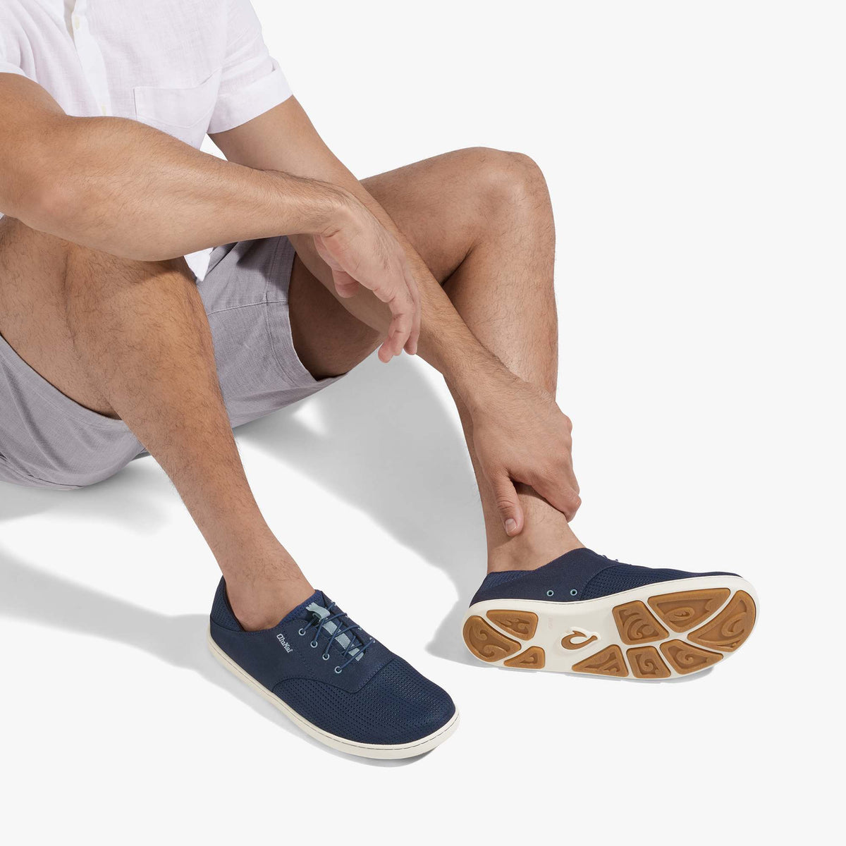 Man wearing navy blue slip-on sneaker with white sole and tan tread pattern, paired with gray shorts.