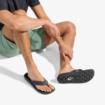 Man wearing black thong sandal with textured sole and gold logo detail.