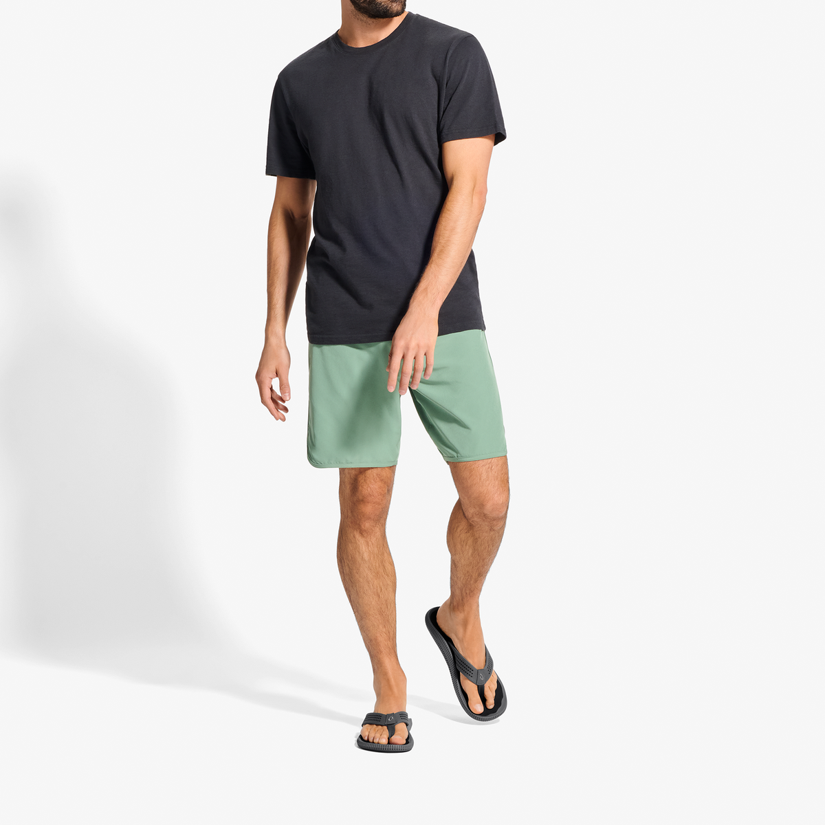 Man wearing black short-sleeve t-shirt, sage green shorts, and black slide sandals.
