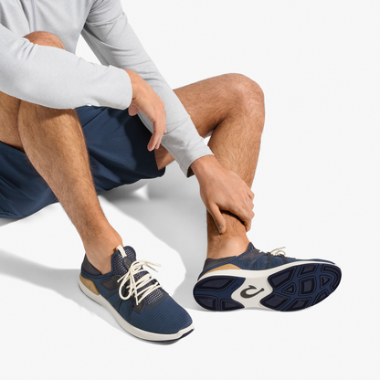 Man wearing white long-sleeve shirt and navy shorts seated, displaying navy and natural lace-up sneaker with white sole.