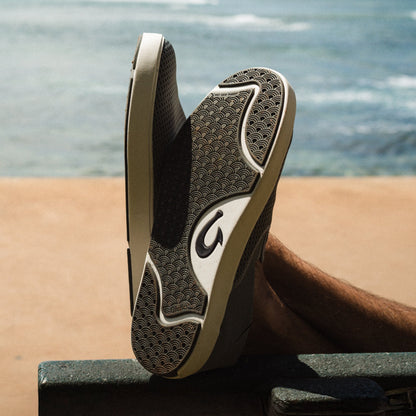 Black and cream sneaker with textured sole and wave pattern design displayed at beach with ocean background.