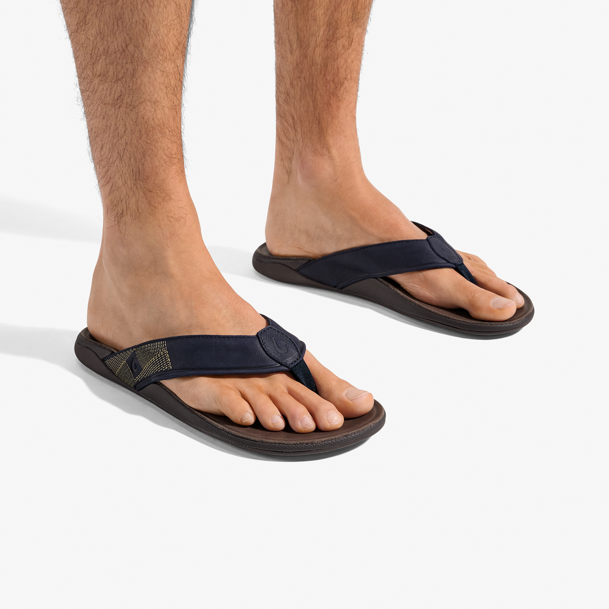 Man wearing dark blue thong sandals with dark brown soles and adjustable straps.