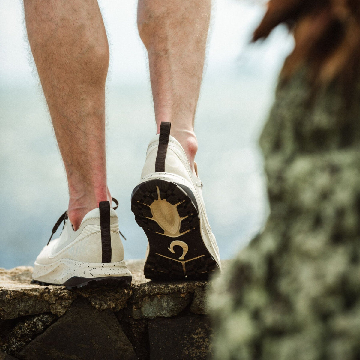 White and black athletic shoes with speckled sole detail worn by person standing on rocky surface.
