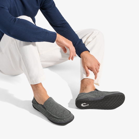 Dark gray slip-on slipper with black sole, worn with navy long-sleeve shirt and white pants.