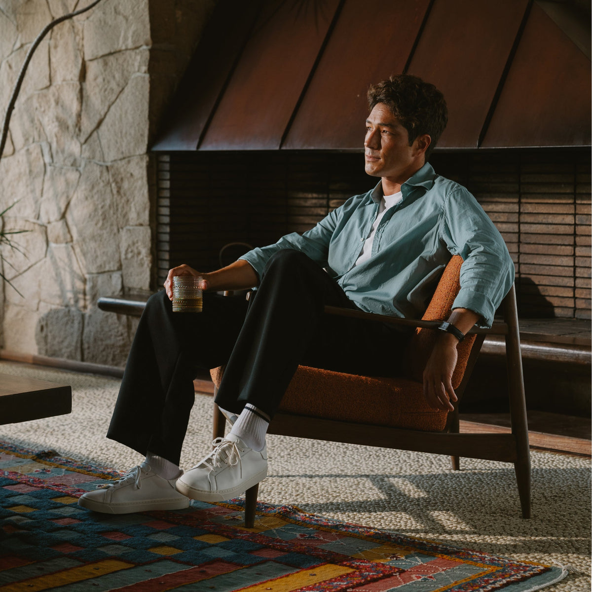 White lace-up sneaker with ribbed crew sock, worn by seated man in casual styling.