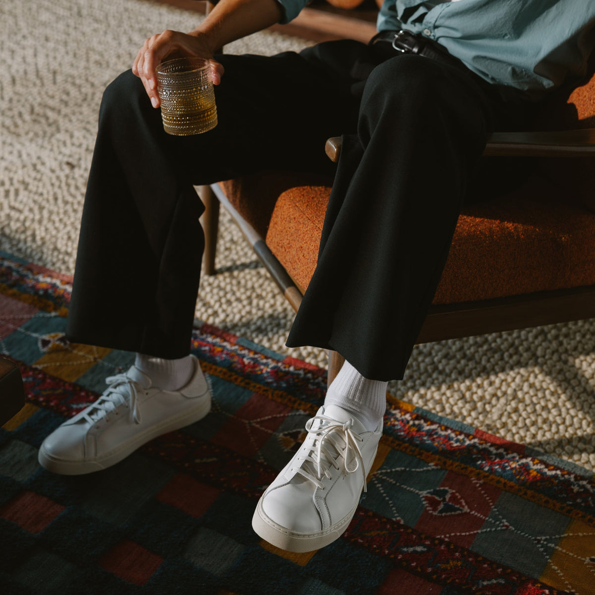 White lace-up sneaker with white sole worn with white socks and black pants.