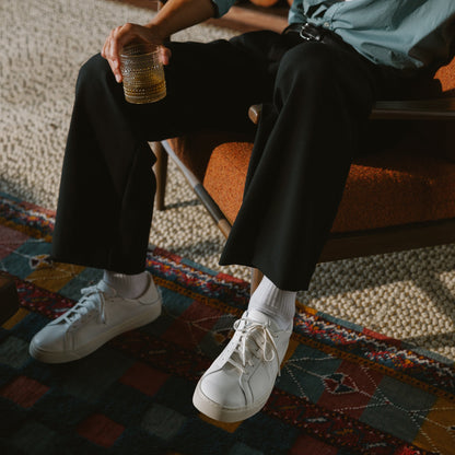 White lace-up sneaker with white sole worn with white socks and black pants.