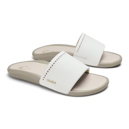 White slide sandals with textured straps and beige soles, shown in pairs from a three-quarter view.