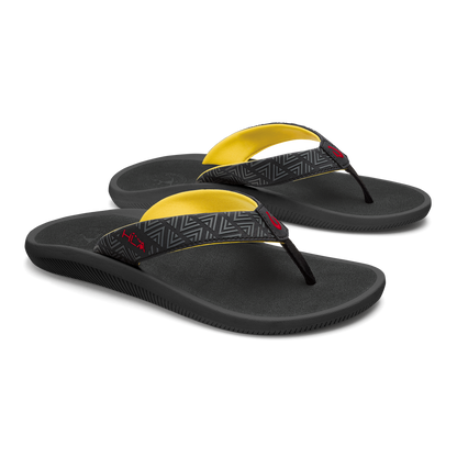 Black flip-flops with yellow arch straps and geometric patterned toe post bands.