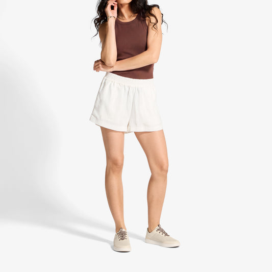 Woman wearing brown sleeveless tank top, white shorts, and cream canvas sneakers.
