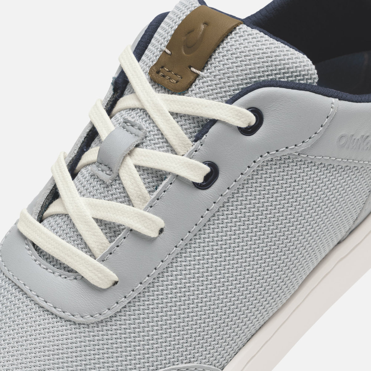 Grey and tan lace-up sneaker with mesh upper, leather overlay, and cream laces, shown from angled side view.