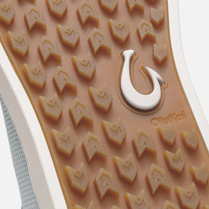 Tan rubber sole with chevron tread pattern, white Olukai heel logo, and grey mesh upper visible at edge.